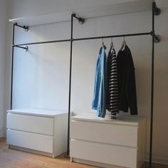 two white drawers with clothes hanging on them in front of a wall mounted coat rack