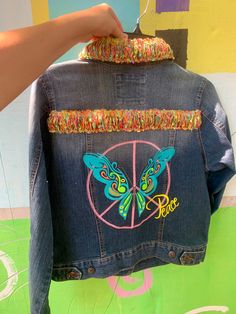 someone is holding up a jacket with the peace sign and butterflies painted on it's back