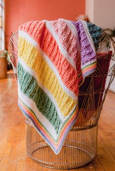 a multicolored blanket sitting on top of a wire basket next to a potted plant