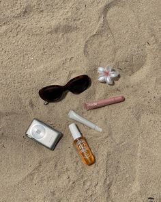 an assortment of personal items layed out on the sand at the beach, including sunglasses, lipstick, and eyeglasses