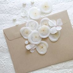 some white flowers are laying on top of an envelope with paper and buttons attached to it