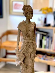 a clay sculpture of a woman holding a flower in her hand and wearing a dress