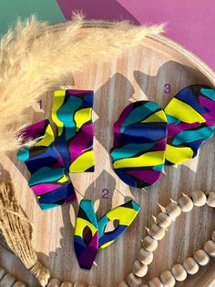 three pieces of colorful fabric sitting on top of a wooden tray next to shells and feathers