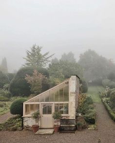 a small building with a bench in front of it and lots of bushes around it