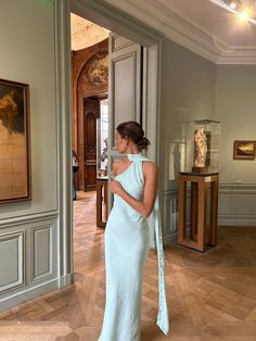 a woman in a blue dress looking at an art piece