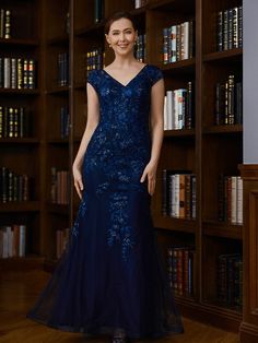 a woman standing in front of bookshelves wearing a blue dress