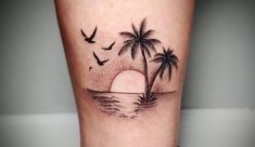 a small palm tree with birds flying over the ocean at sunset on a woman's leg