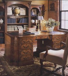 an old fashioned desk with bookshelves and flowers in vases on the table