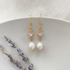 two pairs of earrings sitting on top of a white plate next to lavenders and flowers