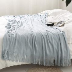 an unmade bed with white sheets and blankets on top of it, next to a potted plant