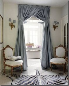 a living room with two chairs and a rug in front of a window that has blue drapes on it