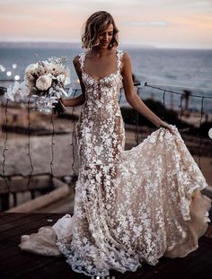 a woman in a wedding dress standing on a deck next to the ocean holding a bouquet