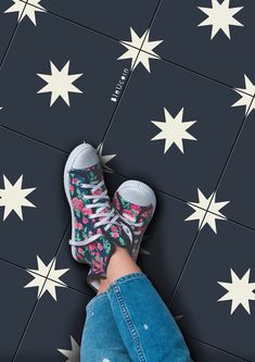 a person's feet in sneakers standing on a tiled floor with stars painted on it