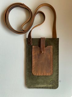 a small green and brown bag hanging on a wall next to a leather belt strap