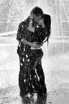 a man and woman kissing under an umbrella in the rain while it rains over them