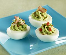 deviled eggs topped with guacamole and bacon on a blue plate, ready to be eaten