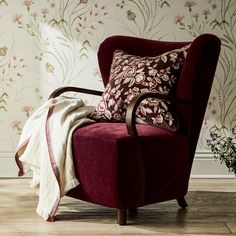 a red chair sitting in front of a wall with flowers on it