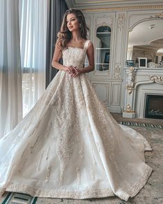 a woman in a wedding dress standing by a window with her hands on her hips