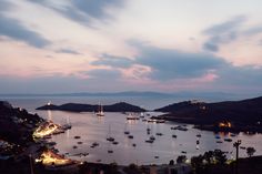 a harbor filled with lots of boats under a cloudy sky at dusk, surrounded by palm trees and mountains