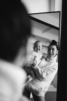 a woman holding a baby in front of a mirror