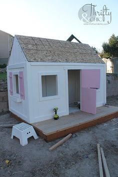 a small white house with pink doors and windows on the front porch is being built