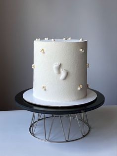 a white cake with baby feet on it sitting on top of a black table next to a metal stand