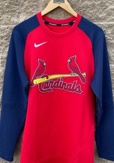 a red and blue baseball jersey with the word cardinals on it hanging up against a stone wall