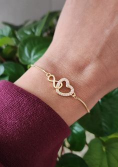 "This 18K gold bracelet is made with gold a linked heart & infinity on a gold adjustable chain. Heart & infinity measures approximately 1\" x .5\" (heart).  The gold brass chain has a ball and joint closure that slides to adjust to the size you need. It can fit almost any size wrist. Slide the ball to the end in order to slide the bracelet over your hand onto your wrist. Slide the ball to tighten it to the size you desire. The remaining chain dangles with 2 small crystals at the ends. This fits most wrist sizes (5-9\")." Gold Bracelet With Adjustable Chain For Valentine's Day Gift, Adjustable Yellow Gold Chain Bracelet For Valentine's Day, Adjustable Heart-shaped Gold Jewelry, Adjustable Gold Dainty Heart Bracelet, Adjustable Gold-plated Bracelet For Anniversary, Adjustable Gold Plated Bracelet For Anniversary, Dainty Adjustable Gold Heart Bracelet, Dainty Gold Chain Bracelet For Mother's Day, Dainty Gold Heart Bracelet Adjustable