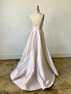 the back of a white wedding dress on a mannequin head stand in front of a wall