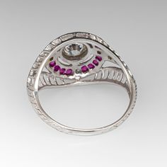 a silver ring with pink stones and white diamonds on the sides, in front of a gray background