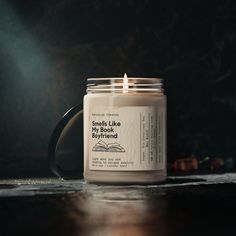 a candle sitting on top of a wooden table next to a black mug with a book in it