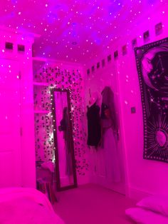 a bedroom with pink lighting and clothes hanging on the closet doors, in front of a mirror