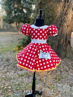 a red and white polka dot dress on a mannequin stand in front of a tree