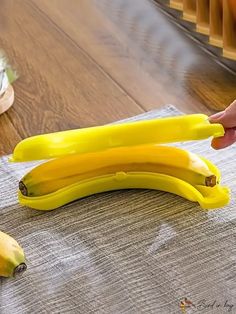 two bananas sitting on top of a wooden table next to a person's hand