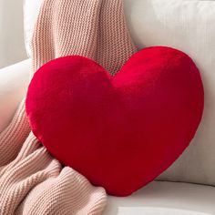 a heart shaped pillow sitting on top of a white couch next to a pink blanket