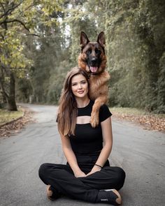 a woman sitting on the ground with her german shepard dog in her lap and smiling at the camera