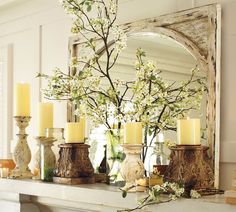 a mantel with candles, flowers and vases on it in front of a mirror