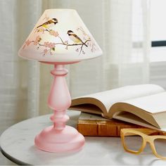 a pink lamp sitting on top of a table next to an open book and glasses