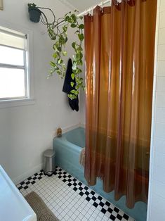 a bathroom with black and white checkered flooring, orange shower curtain, and blue bathtub