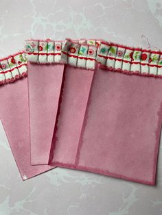 three pink envelopes with white and red trim