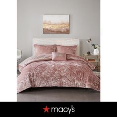 a bed with pink comforter and pillows in a bedroom next to a painting on the wall