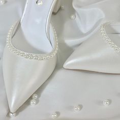 a pair of white high heeled shoes with pearls on the toes and heels are laying next to each other