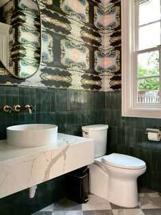 a white toilet sitting next to a sink in a bathroom under a large round mirror