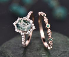 two engagement rings with green and white stones on top of each other in front of a black background