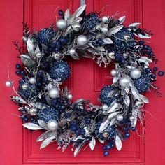 a christmas wreath on a red door with silver and blue ornaments hanging from the front