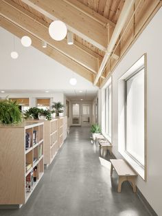 an empty room with benches and plants on the shelves in front of windows, along with bookshelves