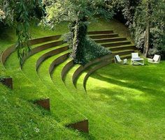 an outdoor area with grass and steps leading up to the tree lined sloped garden