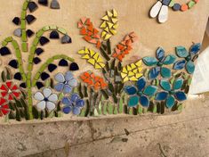 colorful flowers and plants are painted on the side of a stone wall with glass mosaics