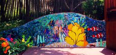 a colorful mosaic fence with flowers and trees in the background, along with an entry way