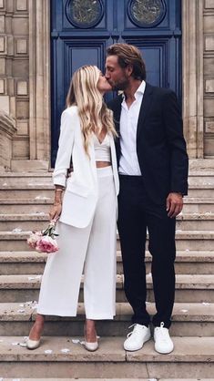 a man and woman are kissing on the steps in front of a blue door with flowers